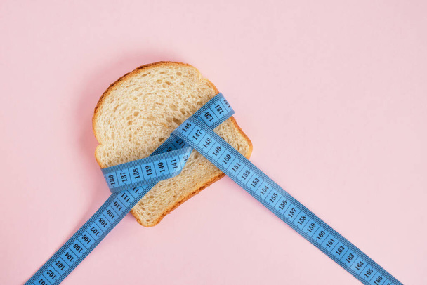 wheat bread slice and blue measuring tape on pink background copy space weight loss concept - Fotó, kép