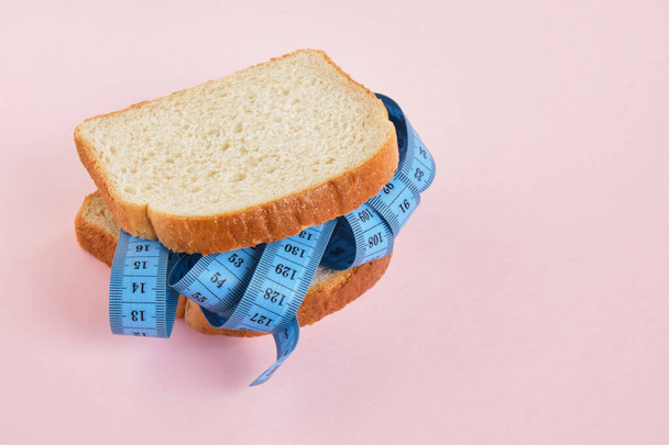 two slices of wheat bread and blue measuring tape on pink background sandwich of bread and measuring tape copy space weight loss and diet concept - 写真・画像