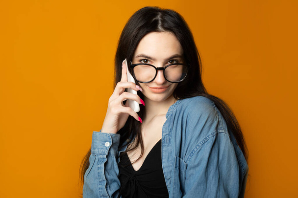 portrait of a beautiful cute woman with glasses on a yellow background with a phone - Photo, Image