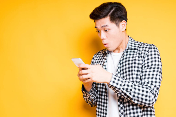 Cute asian guy in a shirt holds a phone in his hands and is surprised by raising his eyebrows - Φωτογραφία, εικόνα