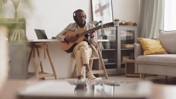 Széles kép jóképű afro-amerikai férfi zenészről, aki fülhallgatót visel otthon, hangstúdióban, és új kislemezt készít akusztikus gitáron. - Felvétel, videó