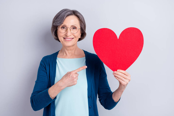 Photo of positive pretty old happy lady point finger large red paper heart romance isolated on grey color background - Fotoğraf, Görsel