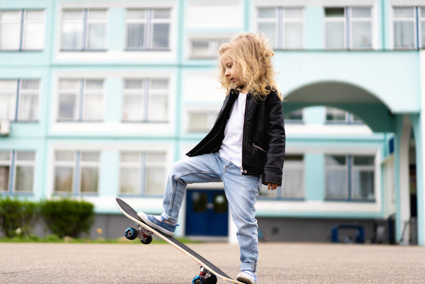 Klein blond meisje op een skateboard in de stad.  - Foto, afbeelding