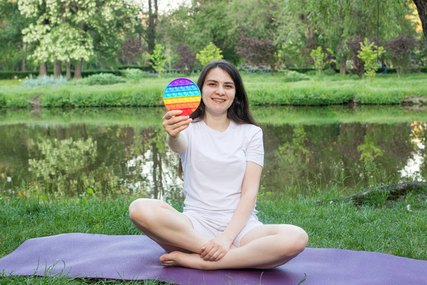 Een vrouw mediteert in de natuur en eet een herbruikbare bubble wrap pop it antistress speelgoed. Omgaan met stress op het werk met Pop it, yoga en meditatie - Foto, afbeelding