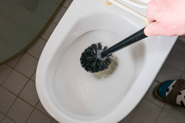Ένας άντρας καθαρίζει μια λεκάνη τουαλέτας με ένα πινέλο. - Φωτογραφία, εικόνα