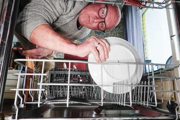 A man fills a dishwasher with a plate. - Photo, Image