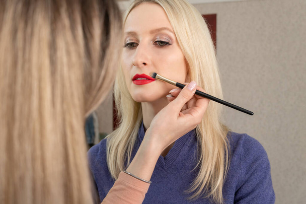Lippenmake-up. Make-up kunstenaar handmatig corrigeert rode lip make-up, afwerking raakt - Foto, afbeelding