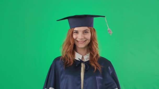 Graduierung online, Mädchen in akademischer Kleidung mit Diplom lächelnd und zeigt Hand zu Klasse und Kamera auf grünem Bildschirmhintergrund, Chroma-Schlüssel - Filmmaterial, Video