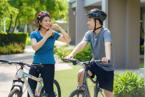 Asiatisches Paar trägt einen Helm, während es sich auf eine Radtour durch seine Nachbarschaft vorbereitet, für die tägliche Gesundheit und das körperliche und geistige Wohlbefinden. - Foto, Bild
