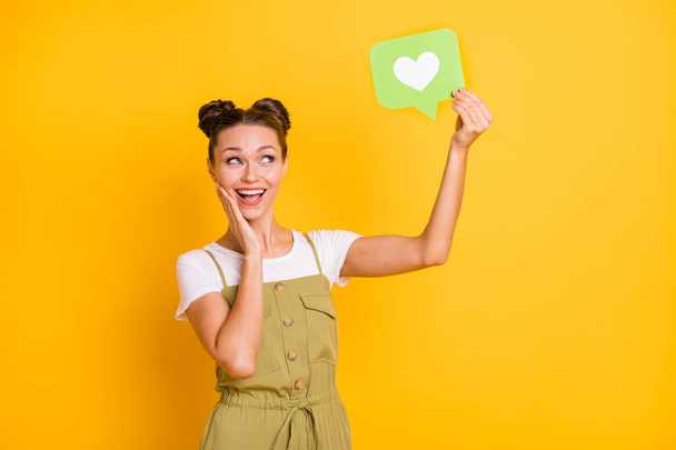 Portrait of attractive trendy amazed cheerful girl holding in hand paper card heart like isolated over bright yellow color background - Photo, image