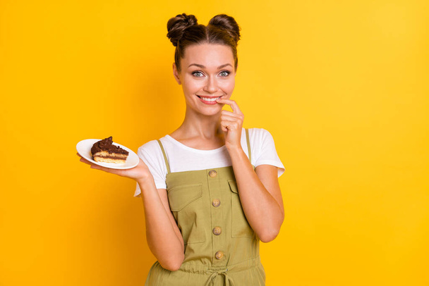 Portrait of attractive cheerful girl holding on palm piece of cake confectionery isolated over bright yellow color background - Фото, зображення