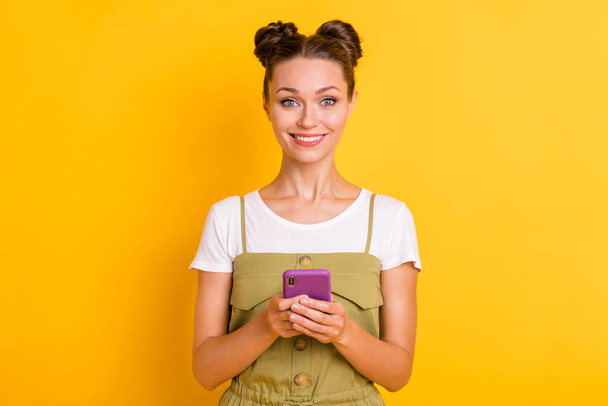Photo of cheerful lady hold telephone look camera shiny toothy smile wear green overall isolated yellow background - Foto, Imagem