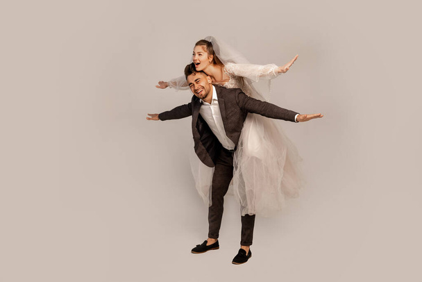 full length view of excited newlyweds having fun isolated on grey with lilac shade - Photo, Image