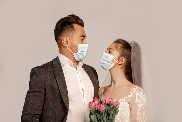 newlyweds in medical masks looking at each other isolated on grey with lilac shade - Foto, immagini