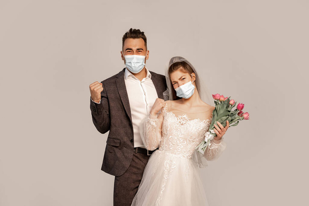 excited newlyweds in protective masks showing yeah gesture isolated on grey - Foto, Imagen