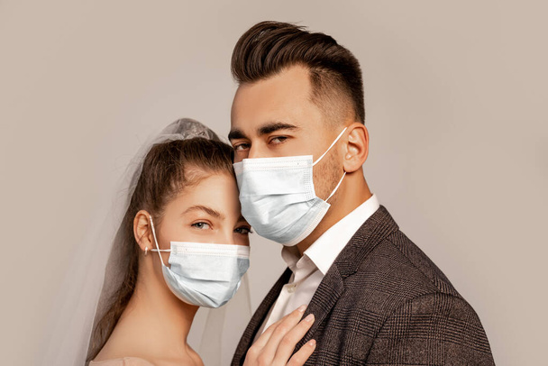 young bride and groom in medical masks looking at camera isolated on grey with lilac shade - Fotografie, Obrázek