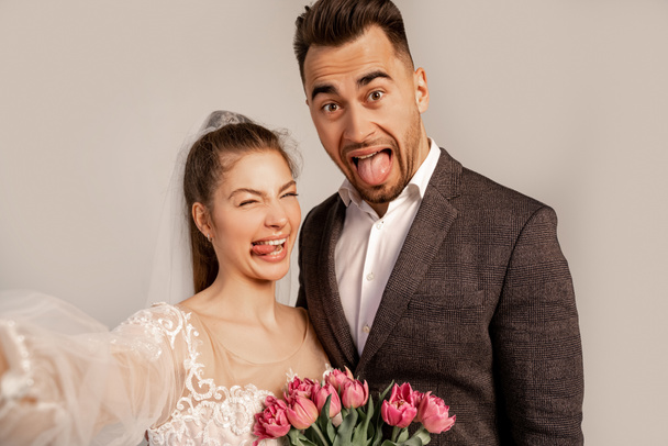 grimacing couple sticking out tongues at camera isolated on grey - Photo, image