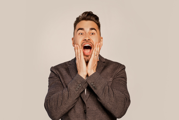 shocked man touching face while screaming isolated on grey - Foto, immagini