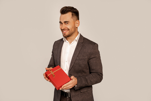 happy man with gift box smiling at camera isolated on grey - Foto, immagini