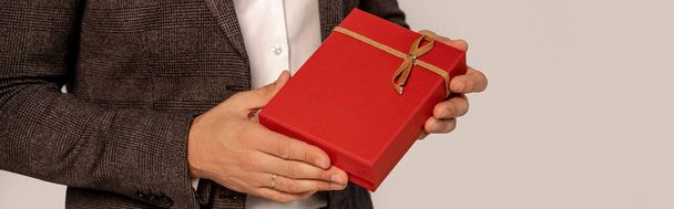 частичный вид человека с красной подарочной коробкой изолированный на сером с сиреневым оттенком, баннер - Фото, изображение