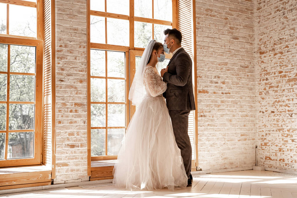 full length view of young newlyweds in protective masks standing near large windows - Foto, Imagen