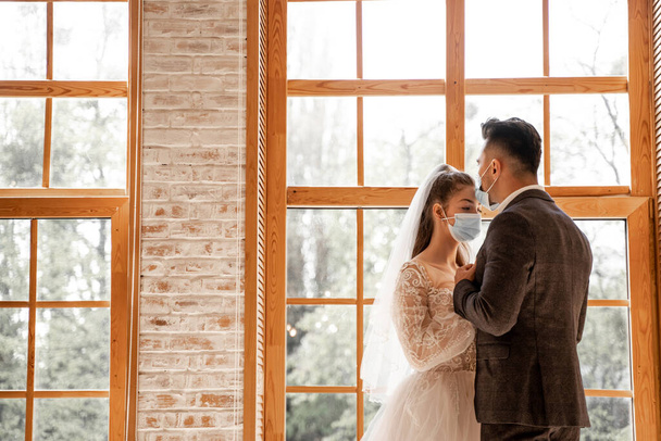 newlyweds in protective masks near large windows at home - Foto, Imagen