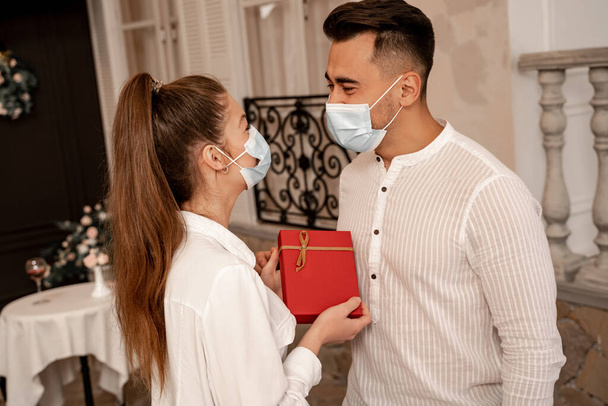 young woman in protective mask holding present near boyfriend in restaurant - Foto, Imagen