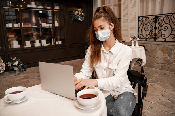 young woman in medical mask working on laptop in cafe - Fotografie, Obrázek