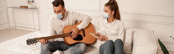 young couple in medical masks playing acoustic guitar and mbira at home, banner - Foto, Imagen