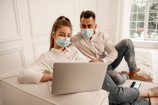 young couple in medical masks watching movie on laptop at home - Φωτογραφία, εικόνα