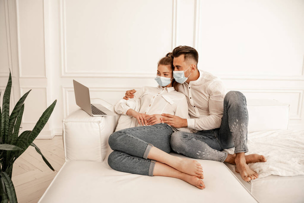 man in medical mask hugging girlfriend while watching movie on laptop - Fotó, kép