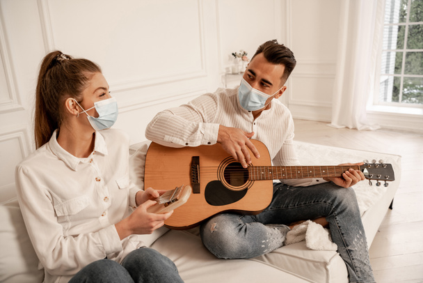 couple in safety masks playing musical instruments in living room - Foto, Imagen