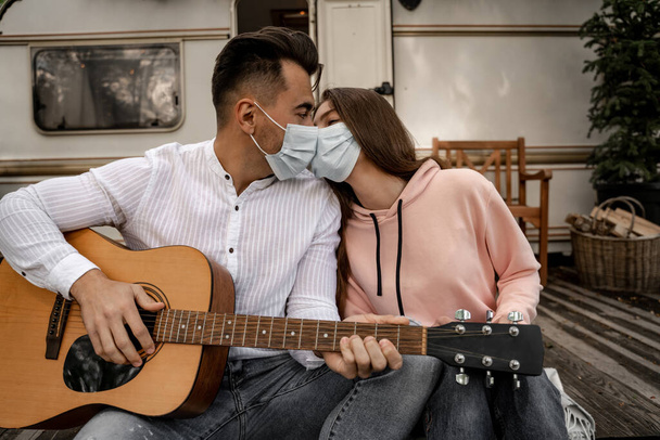 young man in medical mask kissing girlfriend and playing guitar in camping - Φωτογραφία, εικόνα