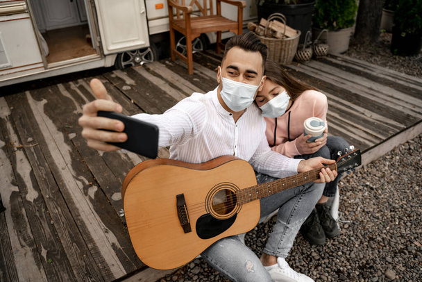 man with guitar taking selfie with girlfriend in medical mask outdoors in camping - Fotó, kép