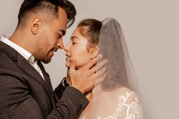 side view of young man touching face of charming bride isolated on grey - Photo, Image