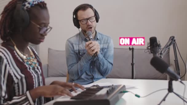 Sulkeminen tyylikäs Afrikkalainen Amerikan naispianisti pelaa syntetisaattori kun valkoihoinen mies laulaa mikrofonissa aikana radio-ohjelma ilmassa - Materiaali, video