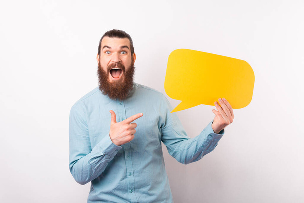 Amazed bearded man screaming and pointing at empty yellow speech bubble. - Photo, Image