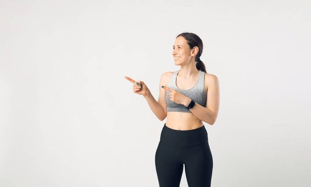 Photo of young fit sport woman in sportswear pointing away and smiling. - 写真・画像