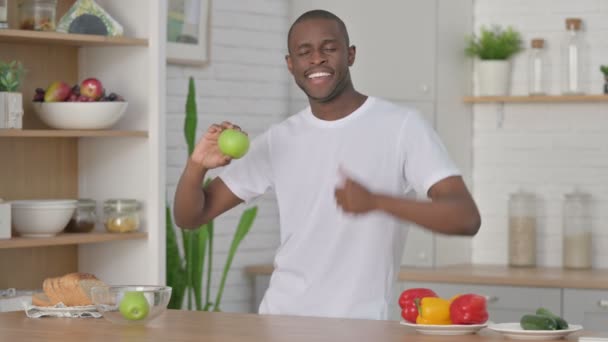 sportivo africano uomo mostra pollici fino mentre tenendo mela in cucina - Filmati, video