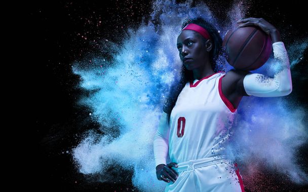 One young woman sportsman basketball player in explosion of colored neon powder isolated on dark background - Foto, immagini