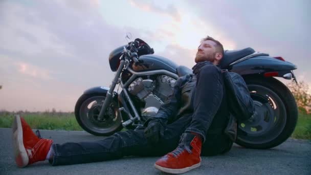 Motociclista de mediana edad con barba se sienta en moto al atardecer - Imágenes, Vídeo