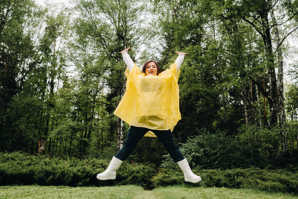 a woman in a yellow raincoat shows emotion and bounces around the park in the summer before the rain. - Photo, image