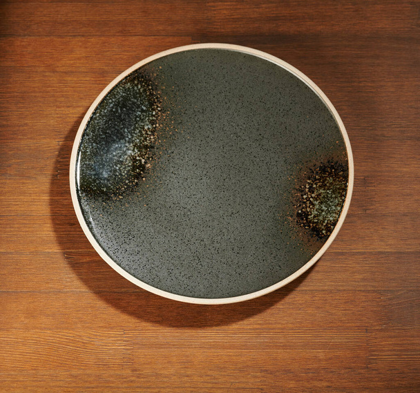 Tmavě šedá prázdná večeře talíř na hnědém dřevěném stole nad horní pohled - Fotografie, Obrázek
