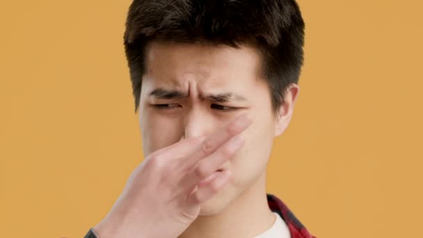 coreano ragazzo pizzicando naso sensazione puzzolente odore su arancio sfondo - Filmati, video