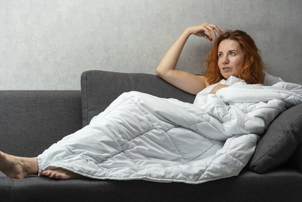 Menina ruiva jovem senta-se coberto com um cobertor branco e fala sobre algo. Conversas na cama. - Foto, Imagem