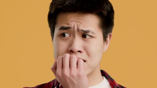 тривожний азіатський хлопець кусає нігті турбуючись про щось, жовтий фон
 - Кадри, відео
