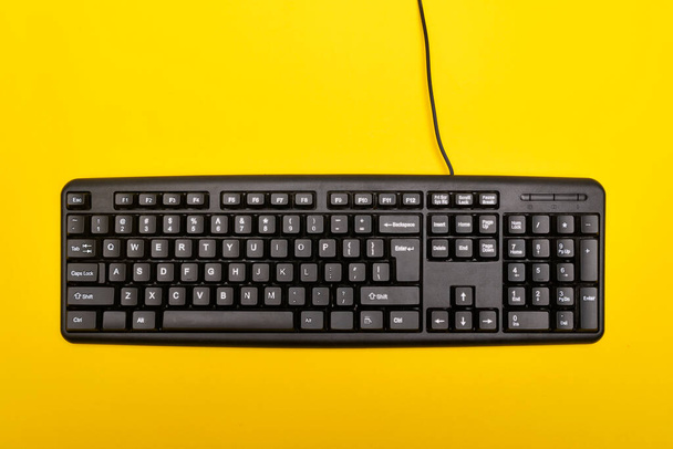 Schwarze Tastatur auf hellgelbem Hintergrund. Verkabelte Computertastatur. Ansicht von oben - Foto, Bild