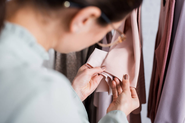 Blurred seamstress looking at sleeves of clothes in atelier  - Photo, Image