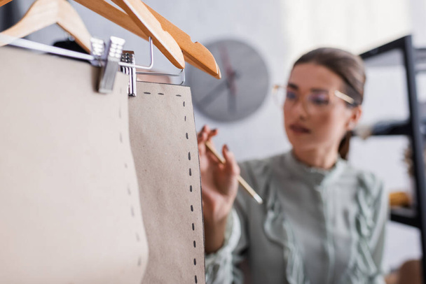 Sewing patters on hangers near blurred seamstress in atelier  - Foto, Imagen