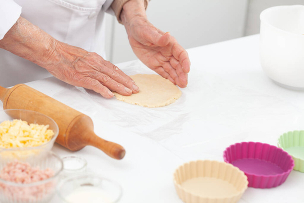 Ηλικιωμένη γυναίκα ετοιμάζεται ζύμη για ένα νόστιμο τυρί και ζαμπόν tartlet - Φωτογραφία, εικόνα